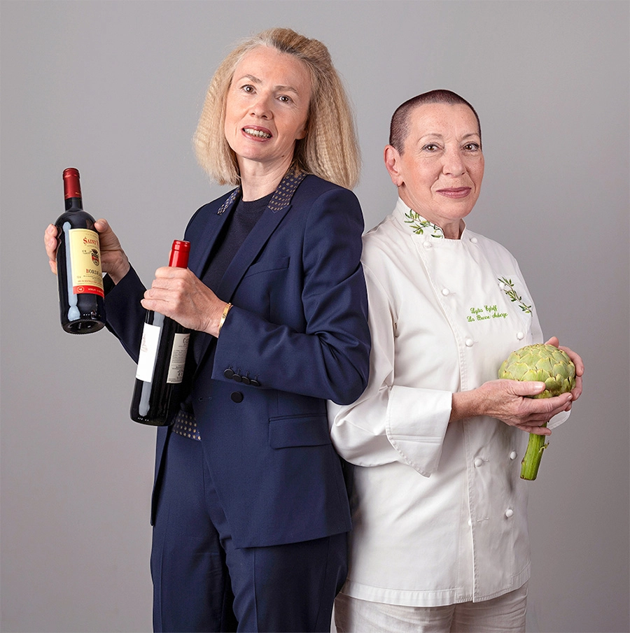 Sophie-mare-Photographe-seingbouse-portrait-corporate-professionel-profil-cv-linkedin-site-internet-13 2 restauratrices dos à dosn une en tailleur bleu, qui tient de bouteilles de vin rouge, une en tenue de cuisinière qui tient un artichaut