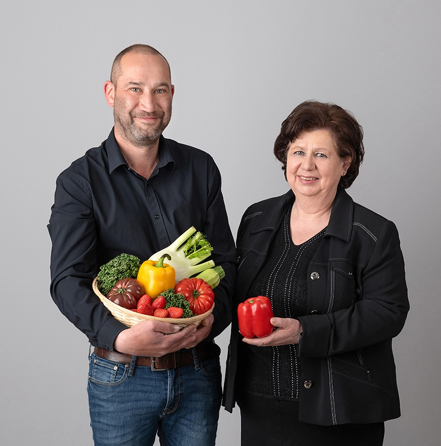 Sophie-mare-Photographe-seingbouse-portrait-corporate-professionel-profil-cv-linkedin-site-internet-15 un homme et une femme en tenue noire sur fond gris. L'homme porte une corbeille de fruits, la femme tient un poivron