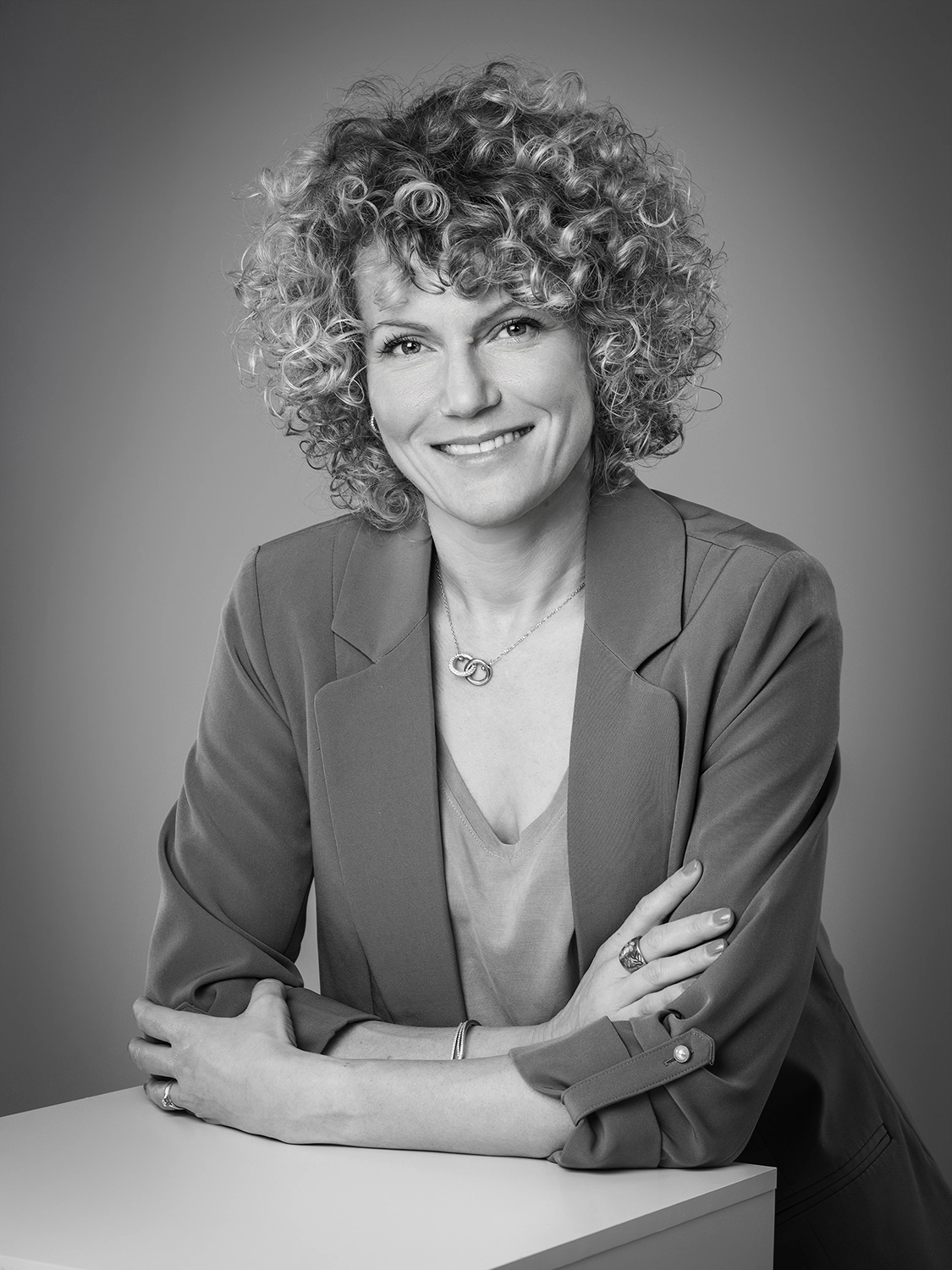 Sophie-mare-Photographe-seingbouse-portrait-corporate-professionel-profil-cv-linkedin-site-internet-36 femme en tailleur, photo noir et blanc, cheveux bouclés, sur fond gris