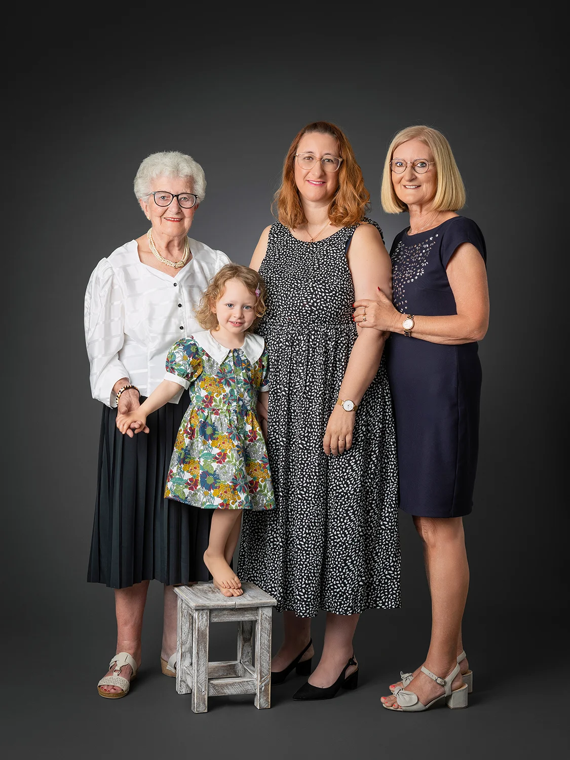 photo générationnelle de 4 femmes : arrière-grand-mère, grand-mère, mère et petite fille en robe sur fond noir