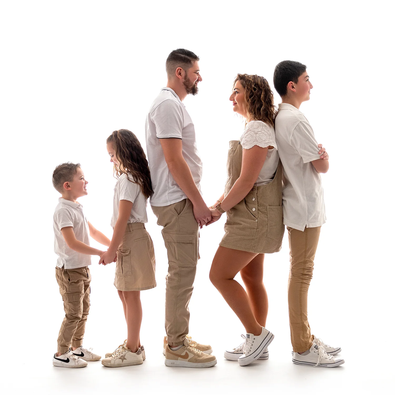 une famille debout, de profil, en tenue beige et chemise blanche, sur fond blanc