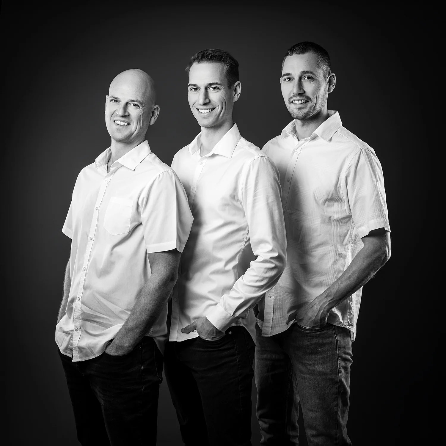 3 frères debout, de profil, en chemise blanche, sur fond noir