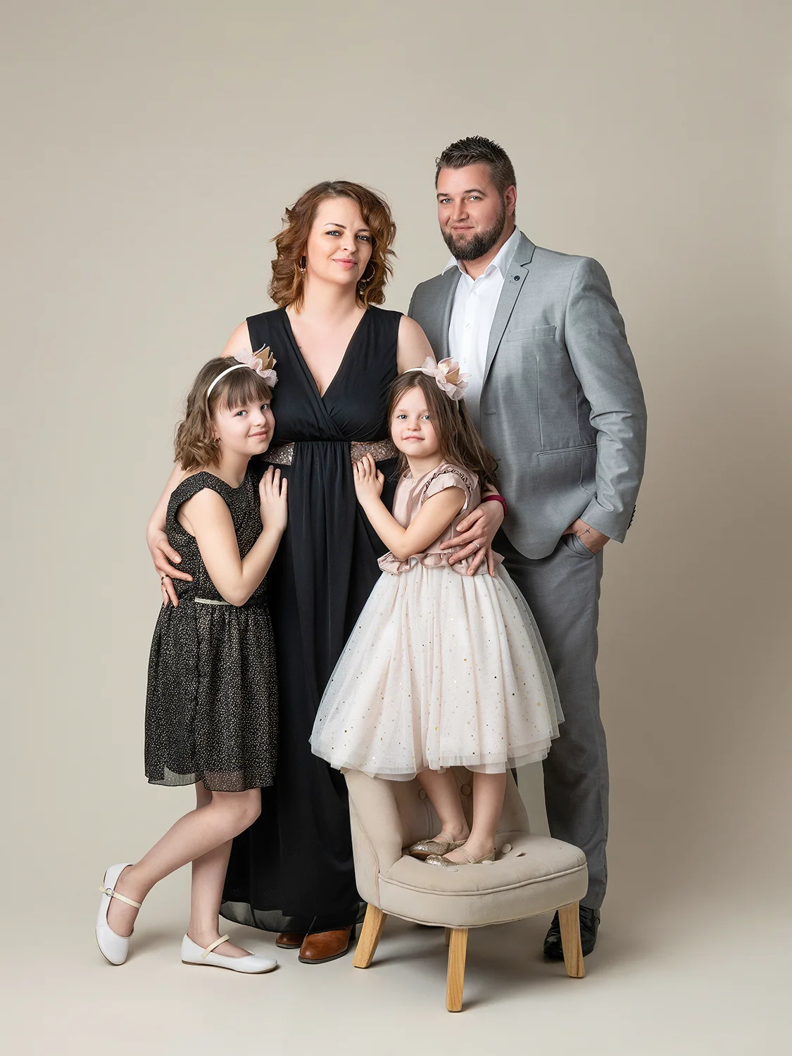 une famille de 4 personnes papa en costume, maman en robe, petites filles en tenues élégantes sur fond blanc naturel