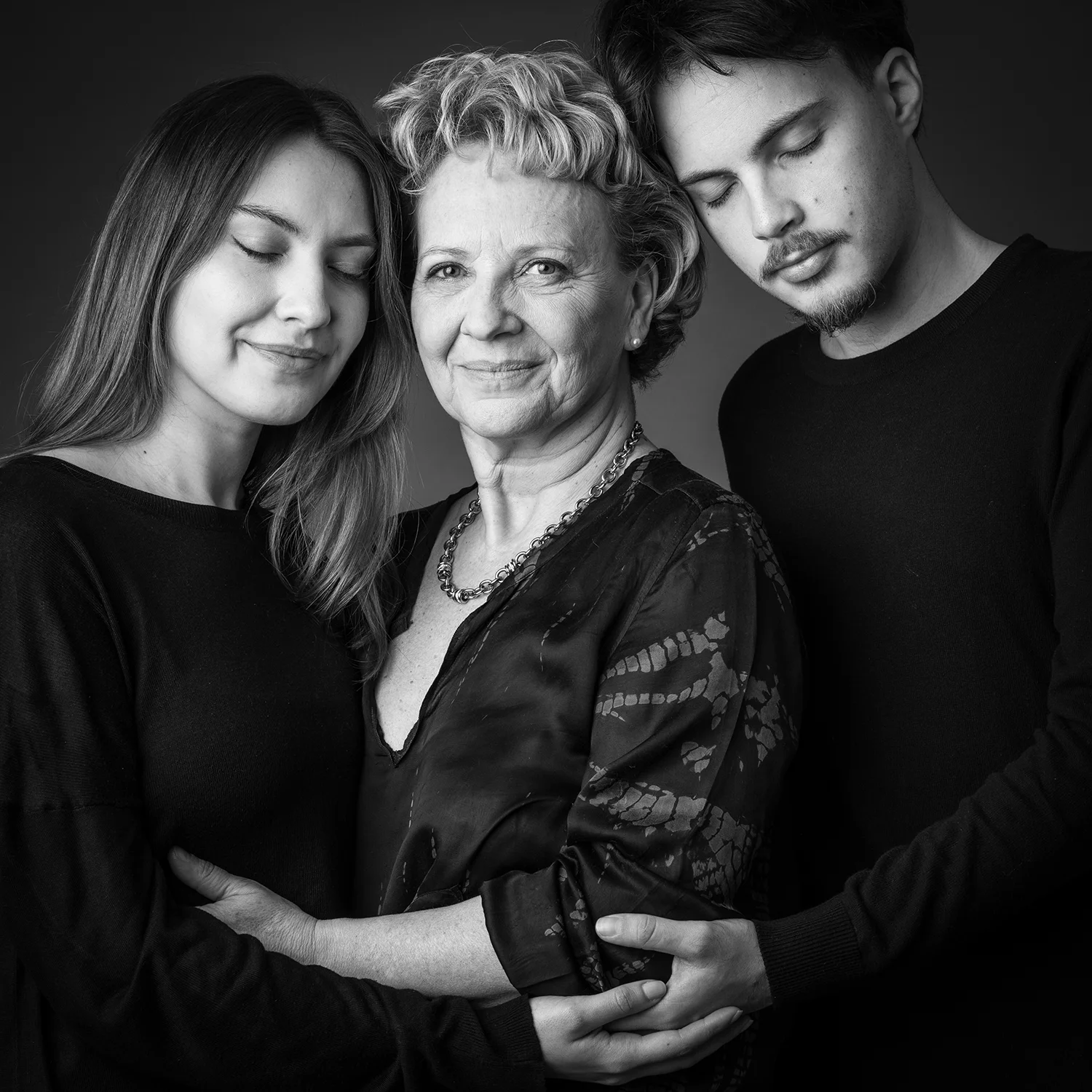 maman et ses 2 enfants avec les yeux fermés sur fond noir avec des tenues noires