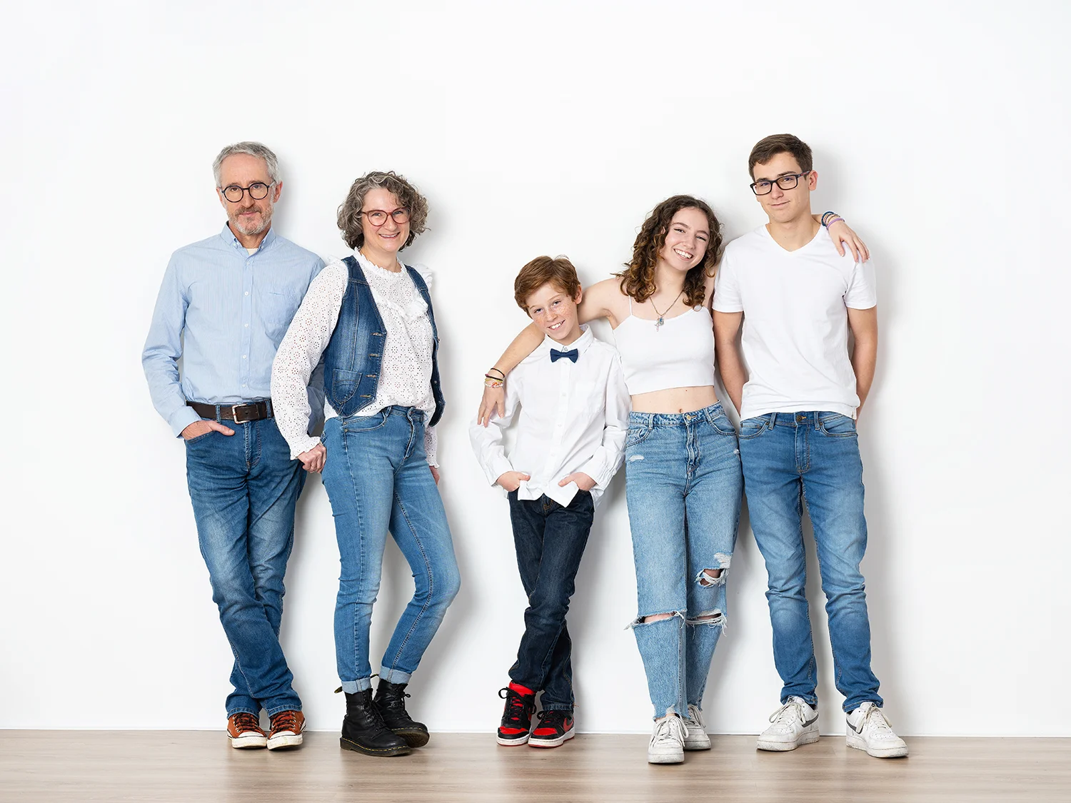 une famille de 5 personnes papa maman et 3 enfants et ados en jean sur mur blanc
