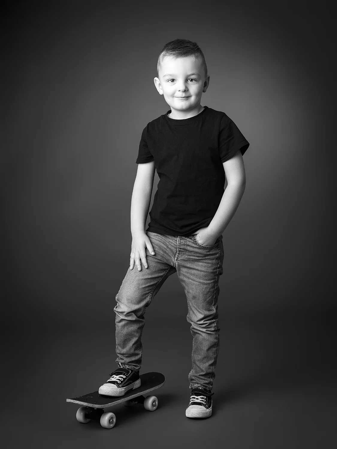studio-seingbouse-photographe-sophie-julien-mare-fratrie-enfant-parents-frere-soeur-portrait-03 garçon en jean et t shirt noir sur fon gris debout avec un pied sur un skate board