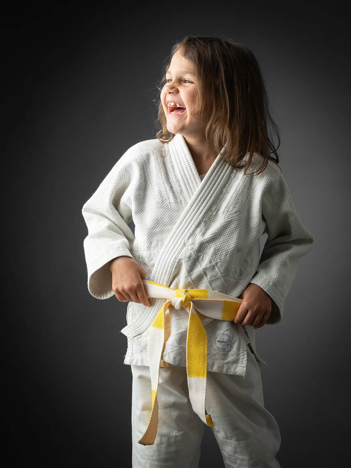 studio-seingbouse-photographe-sophie-julien-mare-fratrie-enfant-parents-frere-soeur-portrait-06 jeune enfant en kimono de judo, ceinture jaune, qui regarde vers la gauche et rit
