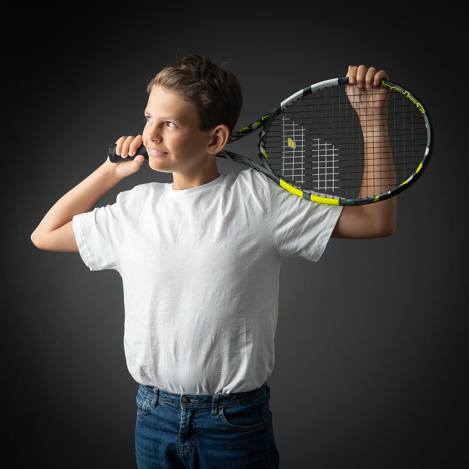 studio-seingbouse-photographe-sophie-julien-mare-fratrie-enfant-parents-frere-soeur-portrait-07 garçon, regard vers la gauche, qui tient une raquette de tennis, fond gris, t shirt blanc