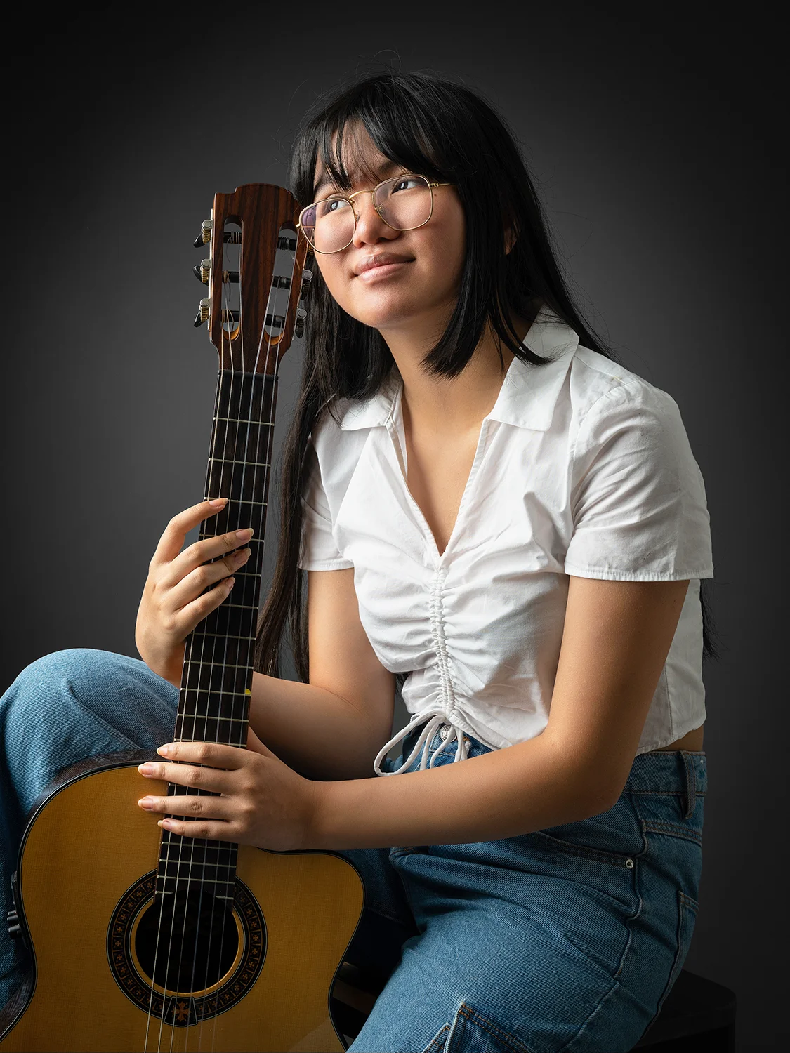 studio-seingbouse-photographe-sophie-julien-mare-fratrie-enfant-parents-frere-soeur-portrait-08 jeune fille ado asiatique haut blanc, qui a son visage contre une guitare, regard lointain vers la gauche