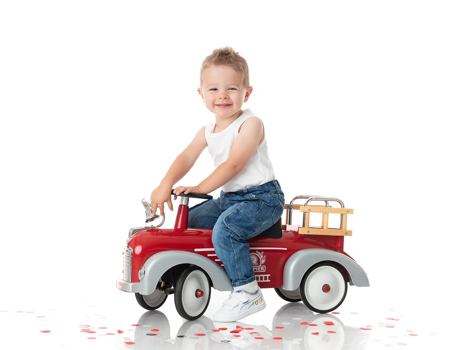 studio-seingbouse-photographe-sophie-julien-mare-fratrie-enfant-parents-frere-soeur-portrait-11 petite garçon sur un camion de pompiers, fond blanc et confettis rouges, en débardeur et jean et fond blanc