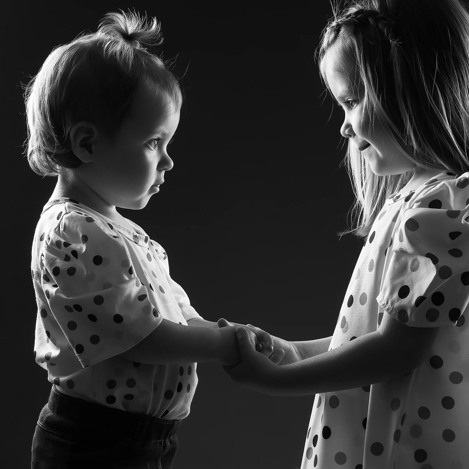 studio-seingbouse-photographe-sophie-julien-mare-fratrie-enfant-parents-frere-soeur-portrait-19 2 soeurs de profil sur fond noir qui se regardent avec des tenues à pois