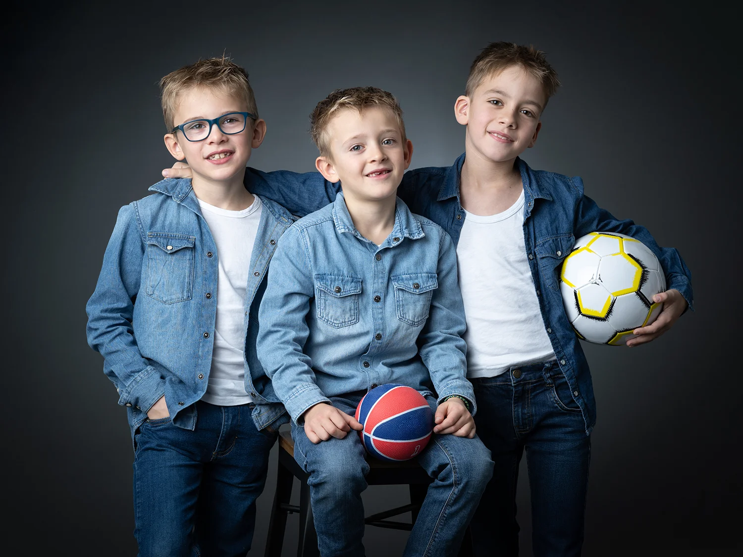 studio-seingbouse-photographe-sophie-julien-mare-fratrie-enfant-parents-frere-soeur-portrait-22 cousins en chemise en jean avec des balls de foot et de hand qui regardent l'objectif, fond noir