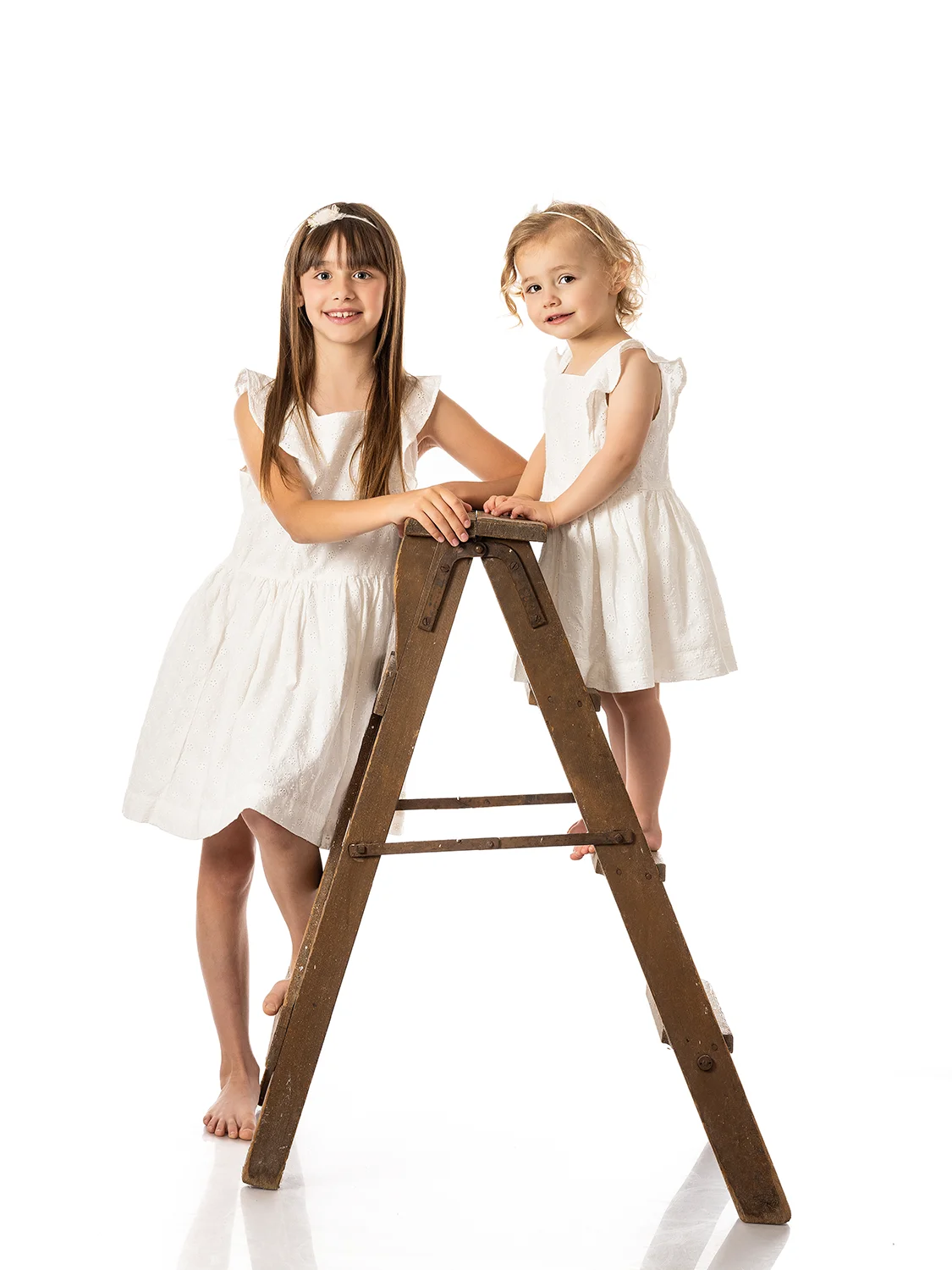 studio-seingbouse-photographe-sophie-julien-mare-fratrie-enfant-parents-frere-soeur-portrait-25 2 sœurs sur une échelle en bois, avec des robes blanches, regard vers l'objectif