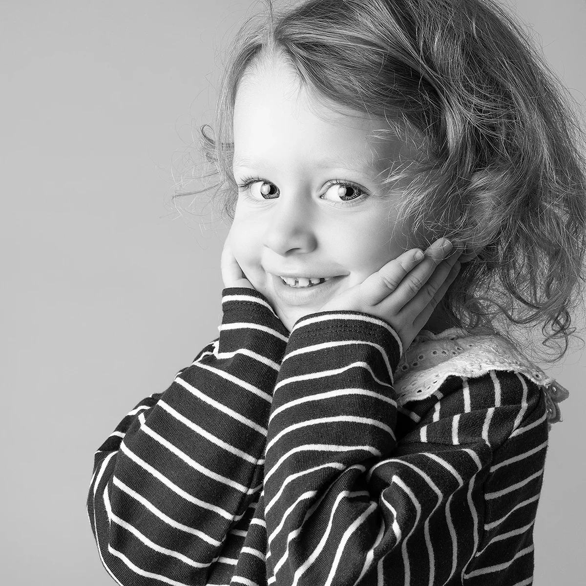 studio-seingbouse-photographe-sophie-julien-mare-fratrie-enfant-parents-frere-soeur-portrait-26 petite fille en marinière, mains sur les joues, qui regarde l'objectif