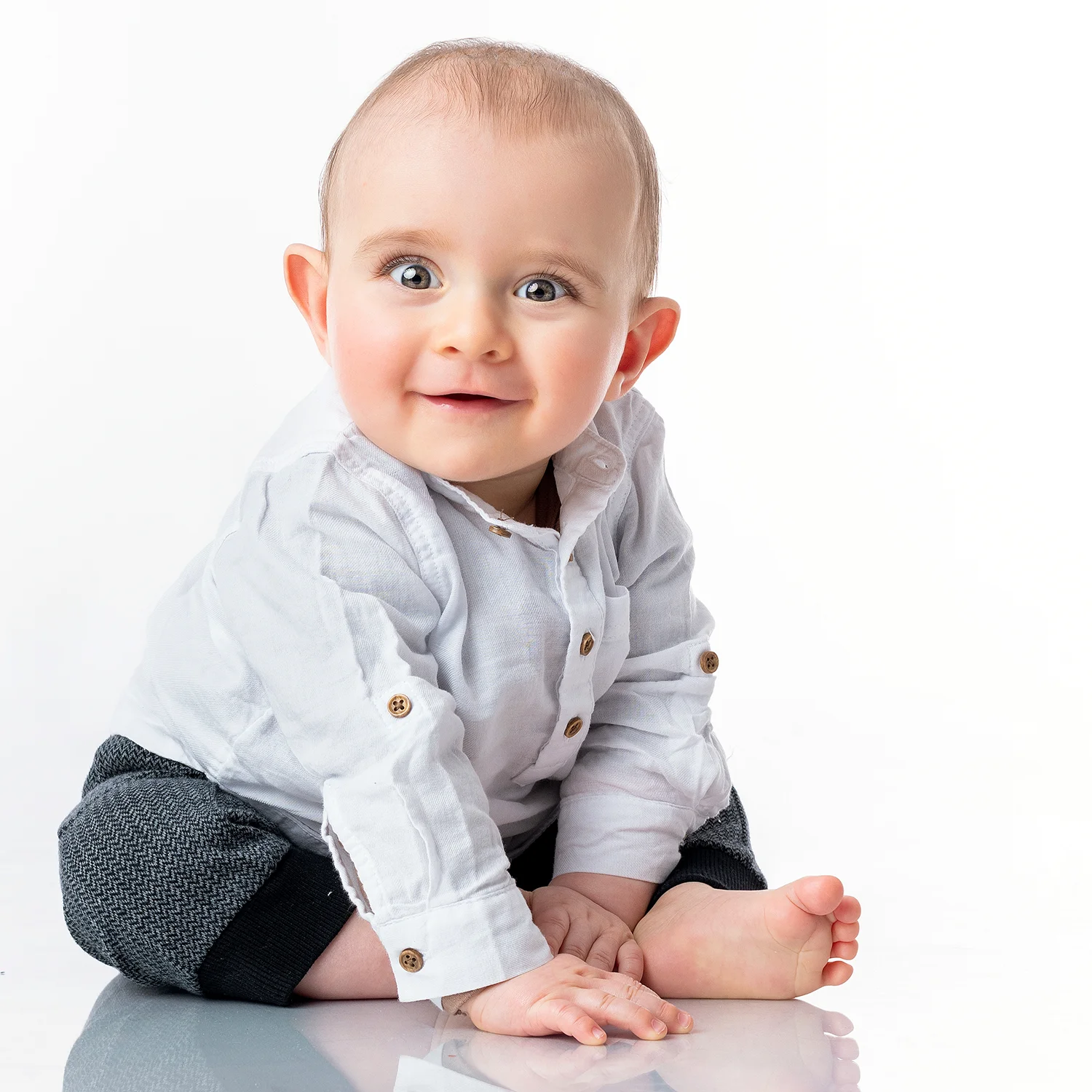 studio-seingbouse-photographe-sophie-julien-mare-fratrie-enfant-parents-frere-soeur-portrait-28 bébé de 10-12 mois qui est assis au sol et qui regarde l'objectif, souriant, avec une chemise, sur fond blanc