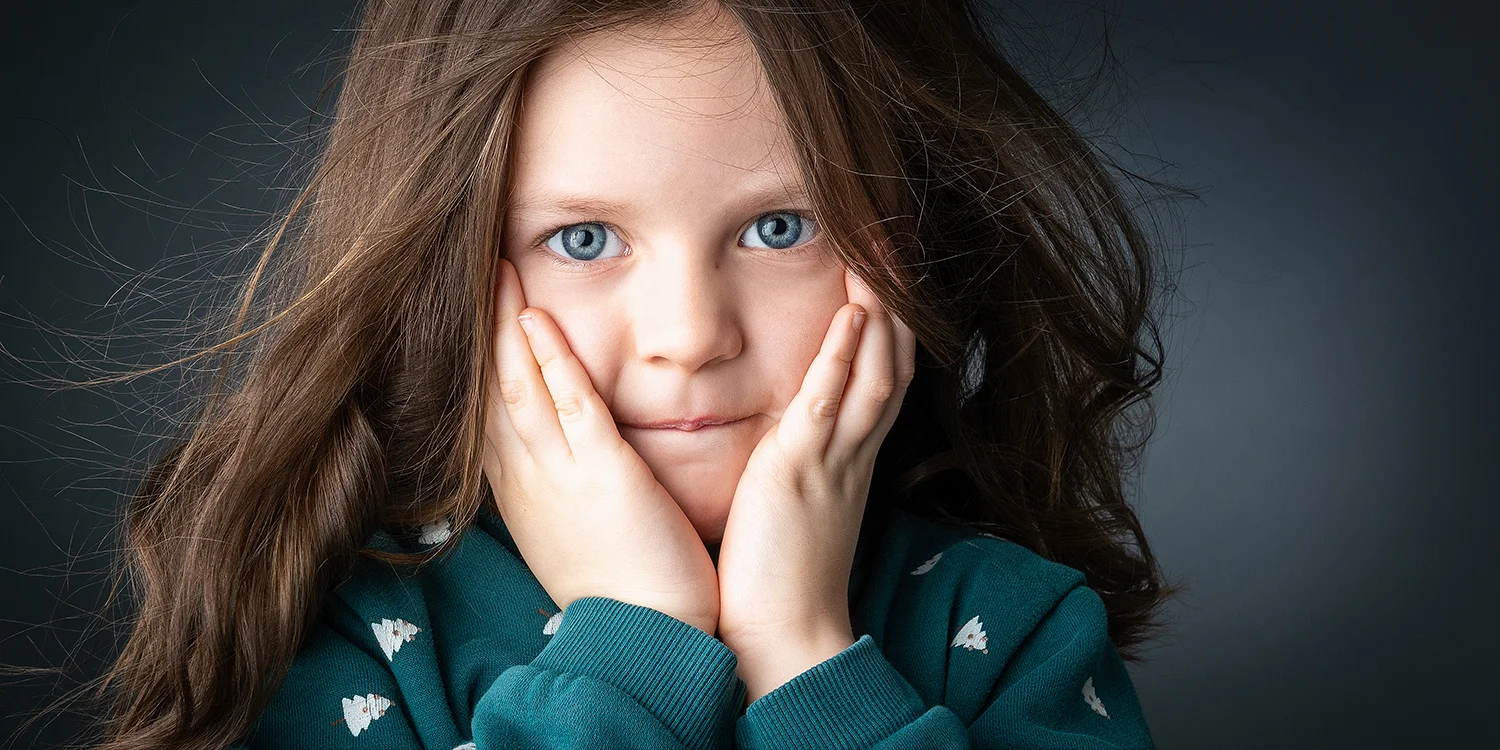 studio-seingbouse-photographe-sophie-julien-mare-fratrie-enfant-parents-frere-soeur-portrait-34 petite fille, mains sur les joues, cheveux qui volent, avec un pull vert, des yeux verts et un fond vert