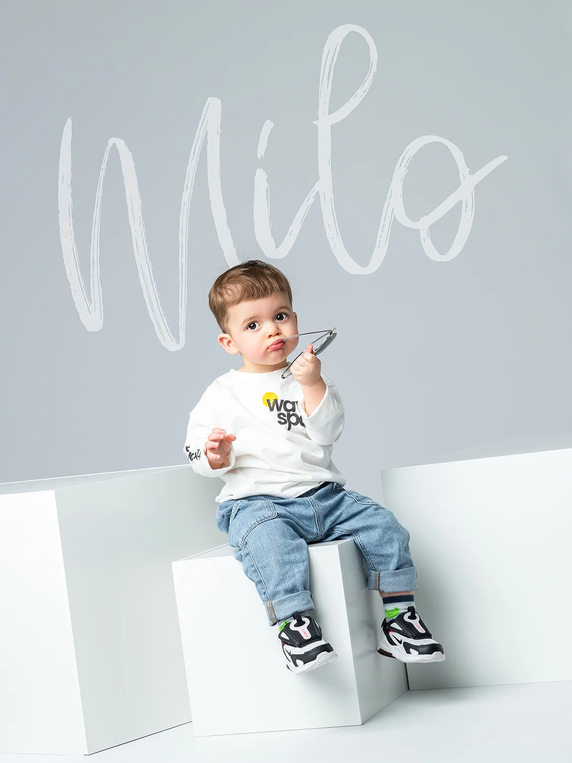 studio-seingbouse-photographe-sophie-julien-mare-fratrie-enfant-parents-frere-soeur-portrait-36 petit garçon avec lunettes de soleil qui fait une grimace, assis sur des cubes blancs, avec un fond gris clair