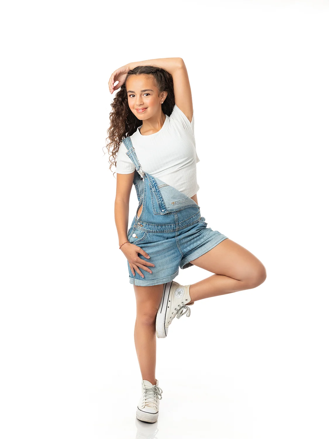 studio-seingbouse-photographe-sophie-julien-mare-fratrie-enfant-parents-frere-soeur-portrait-41 jeune fille en converse et salopette en jean et t shirt blanc qui lève une jambe, sur fond blanc