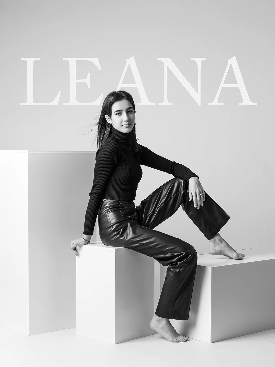 studio-seingbouse-photographe-sophie-julien-mare-fratrie-enfant-parents-frere-soeur-portrait-42 jeune ado en pantalon cuir noir qui regarde l'objectif assise sur des cubes blancs sur fond gris