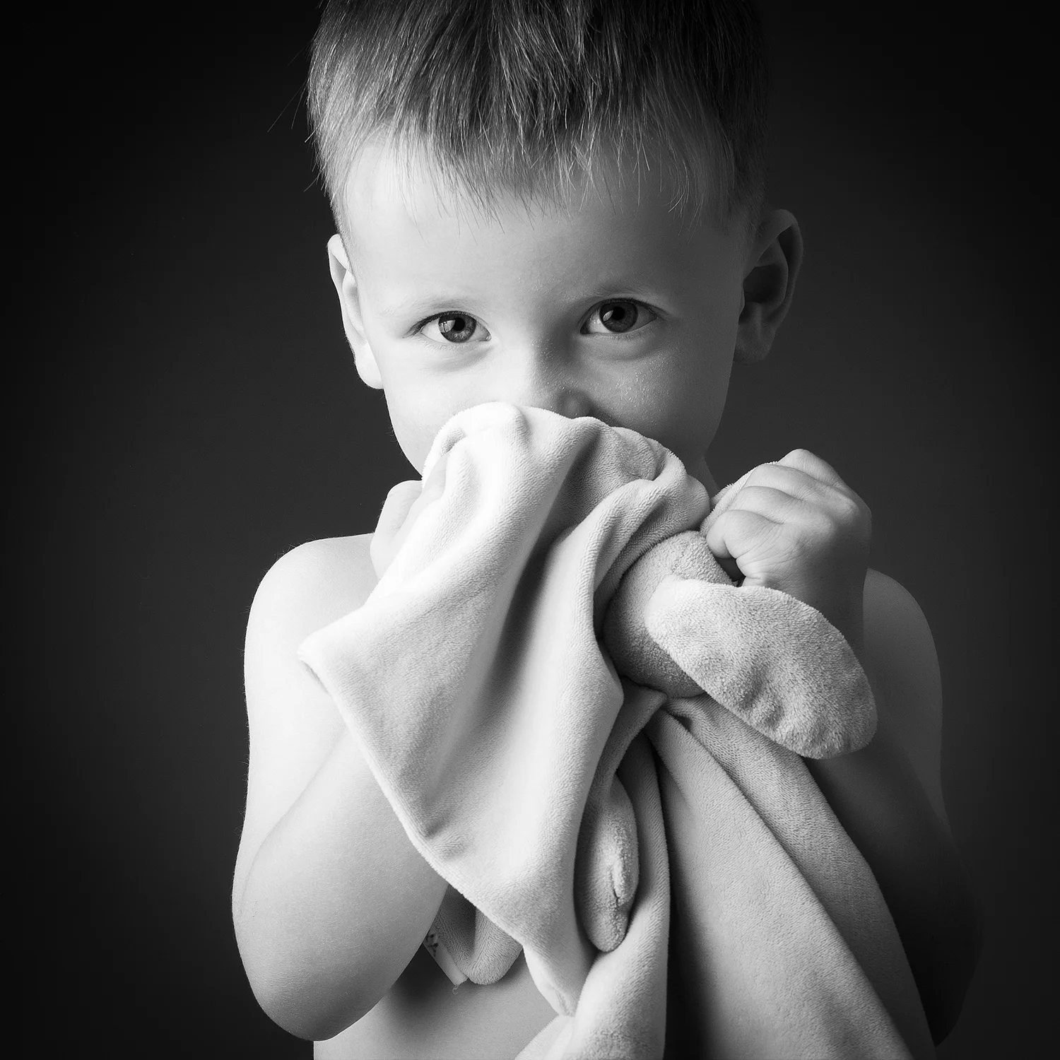 studio-seingbouse-photographe-sophie-julien-mare-fratrie-enfant-parents-frere-soeur-portrait-43 petit garçon torse nu qui sent son doudou et qui regarde l'objectif sur fond noir