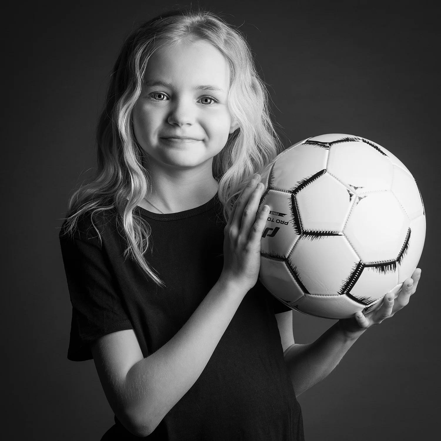 studio-seingbouse-photographe-sophie-julien-mare-fratrie-enfant-parents-frere-soeur-portrait-46 fille de 9 ans avec une balle de foot dans les mains, t-shirt noir qui regarde l'objectif sur fond noir