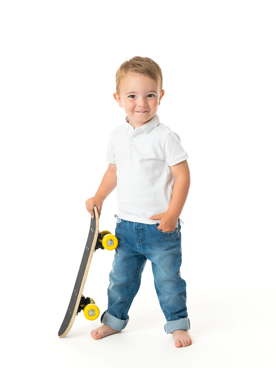 studio-seingbouse-photographe-sophie-julien-mare-fratrie-enfant-parents-frere-soeur-portrait-50 petit garçon en jean et polo blanc qui tient un skate board en main et main dans la poche sur fond blanc