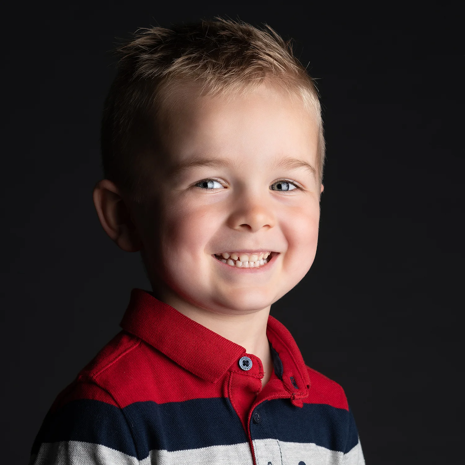 studio-seingbouse-photographe-sophie-julien-mare-fratrie-enfant-parents-frere-soeur-portrait-56 petit garçon blond souriant sur fond noir avec pull rouge