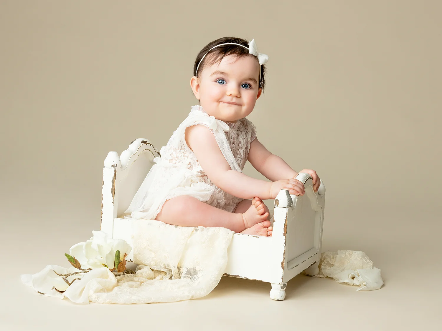 studio-seingbouse-photographe-sophie-julien-mare-fratrie-enfant-parents-frere-soeur-portrait-65 bébé fille sur un lit en bois avec une tenue en dentelle sur fond beige naturel