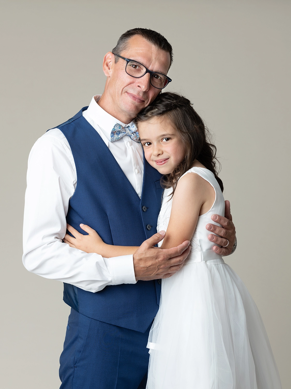 studio-sophie-mare-mariage-photos-seingbouse-merlebach-portrait-05 une petite fille en robe blanche et son papa en costume bleu sur fond beige naturel