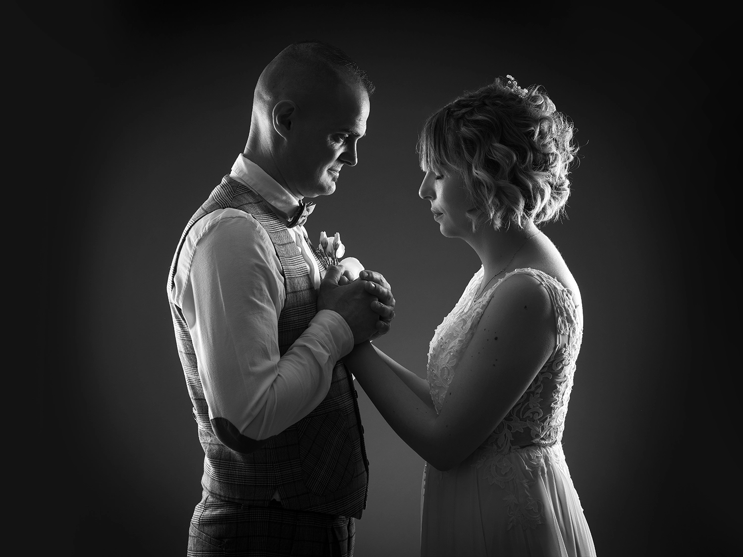 studio-sophie-mare-mariage-photos-seingbouse-merlebach-portrait-17 un couple de mariée en noir et blanc sur fond noir qui se tiennent les mains. La mariée a les yeux fermés, le marié la regarde tendrement.