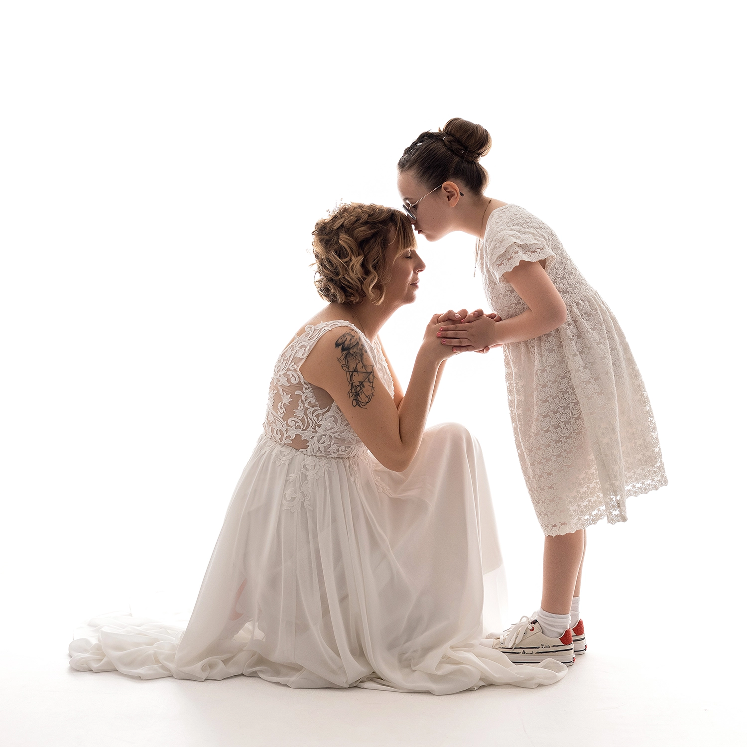 studio-sophie-mare-mariage-photos-seingbouse-merlebach-portrait-20 une mariée en blanc et sa fille en blanc, la mariée est accroupie et les yeux fermés. sur fond blanc