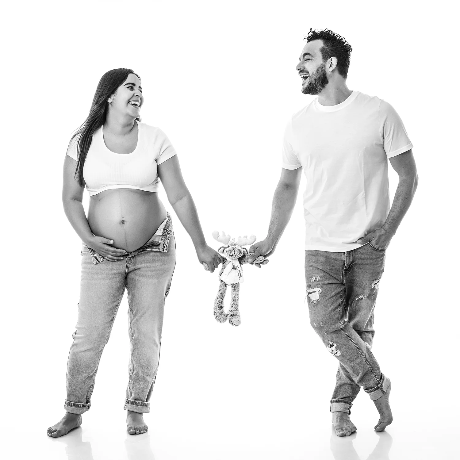 studio-seingbouse-photographe-sophie-julien-mare-grossesse-enceinte-parents-bebe-naissance-shooting-07 une future maman et un futur papa qui se regardent et rient et qui tiennent dans leur main une peluche, sur fond banc