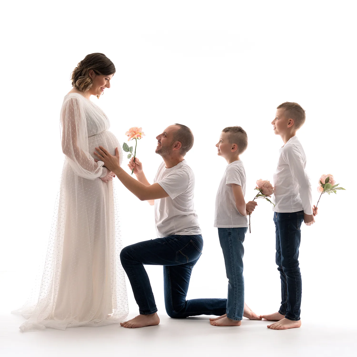 studio-seingbouse-photographe-sophie-julien-mare-grossesse-enceinte-parents-bebe-naissance-shooting-22 une femme enceinte en robe blanche avec un homme et 2 enfants qui tiennent des fleurs dans les mains, sur fond blanc